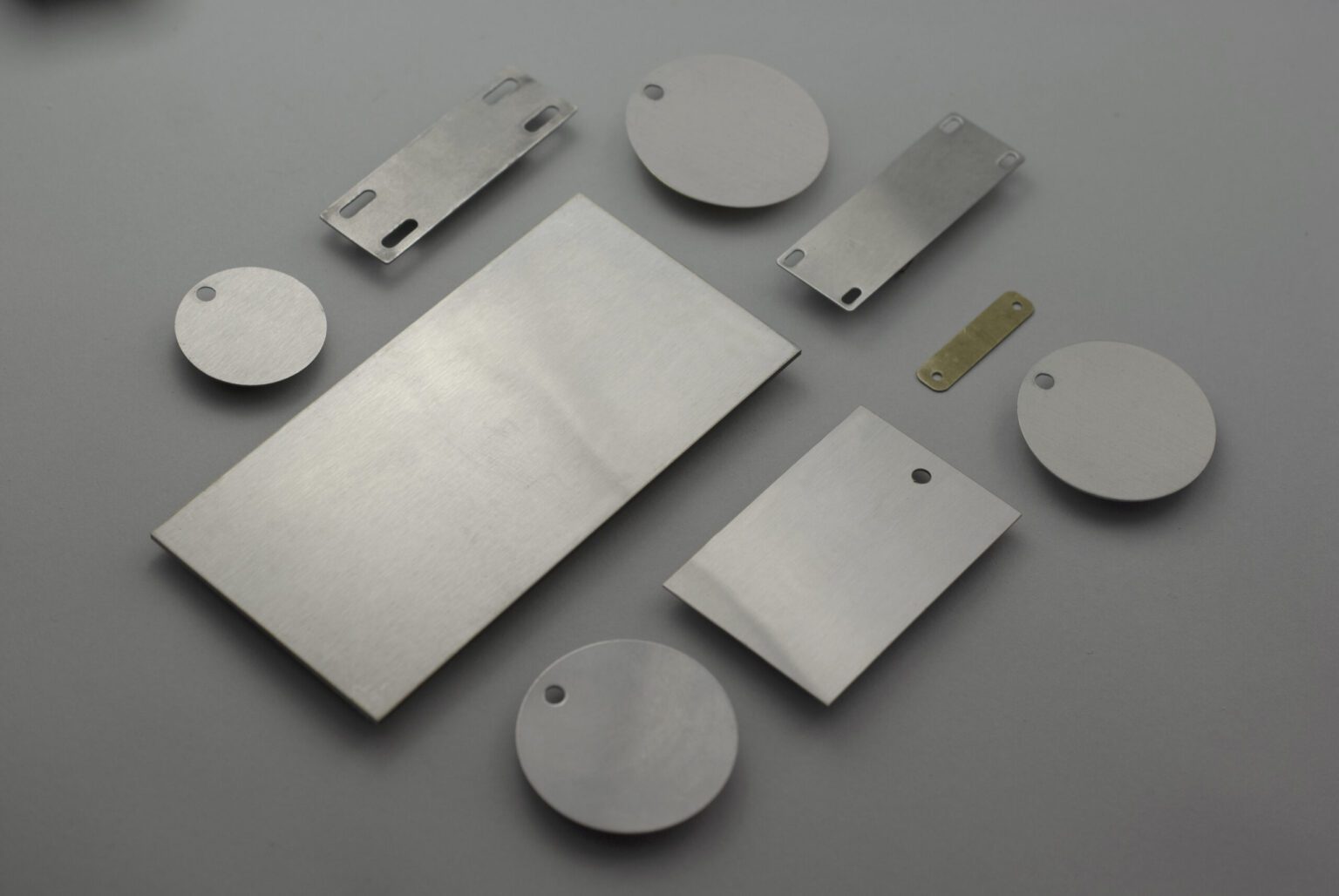 A variety of different size and shape stainless steel conduit tags are displayed nicely against a clean gray background they are all blank the material is shiny