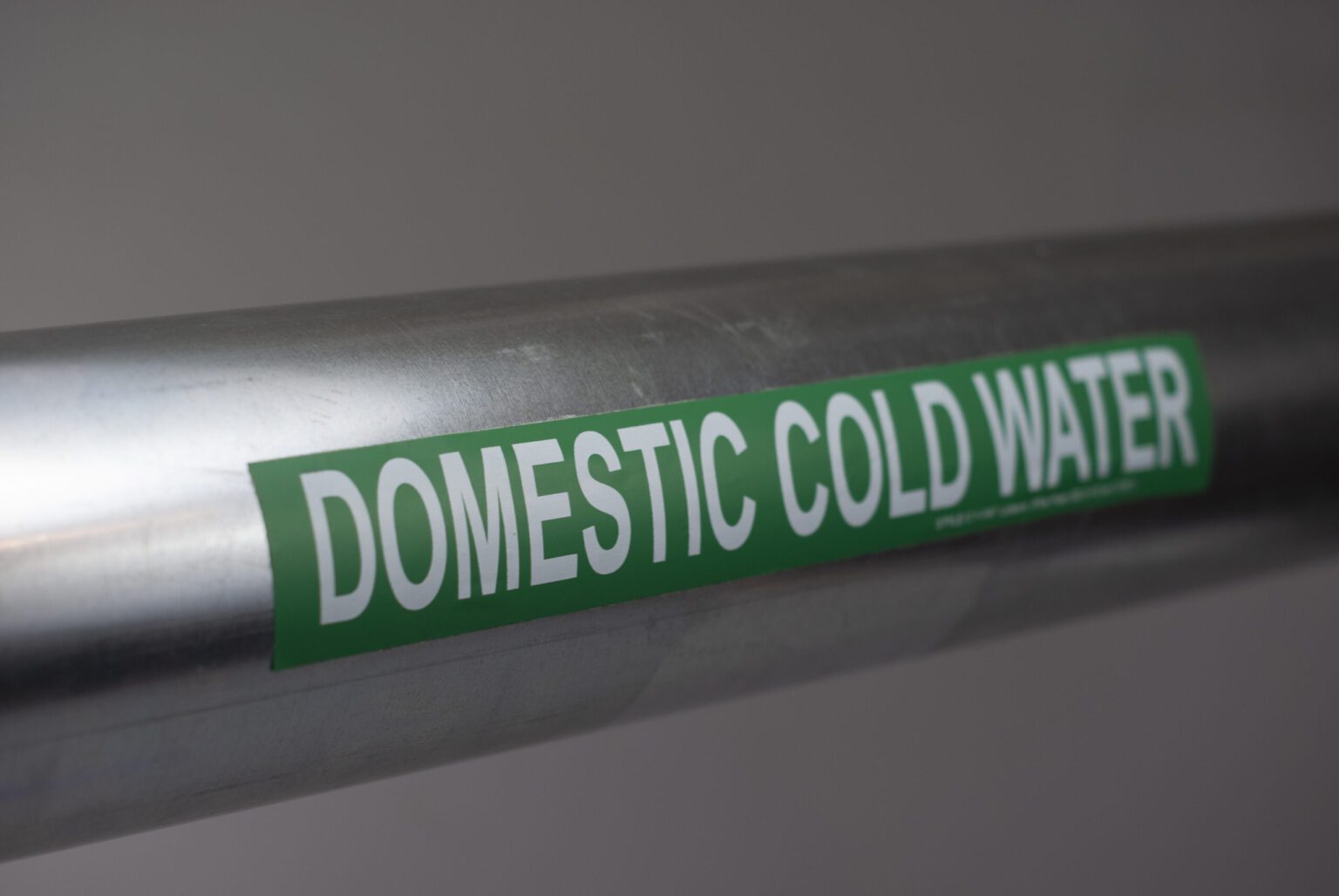 A close up of a steel pipe with a green adhesive pipe marker sticker applied. The Legend reads "domestic cold water"