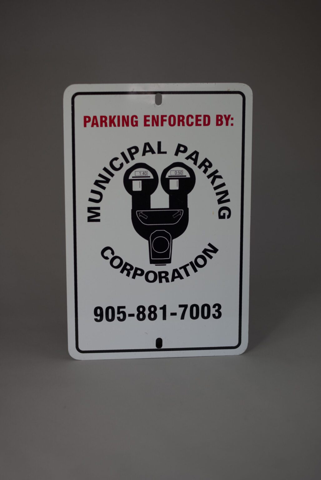 A white road sign that reads parking enforced by Municipal parking Corporation with a icon of a parking meter in the middle there is a phone number at the bottom