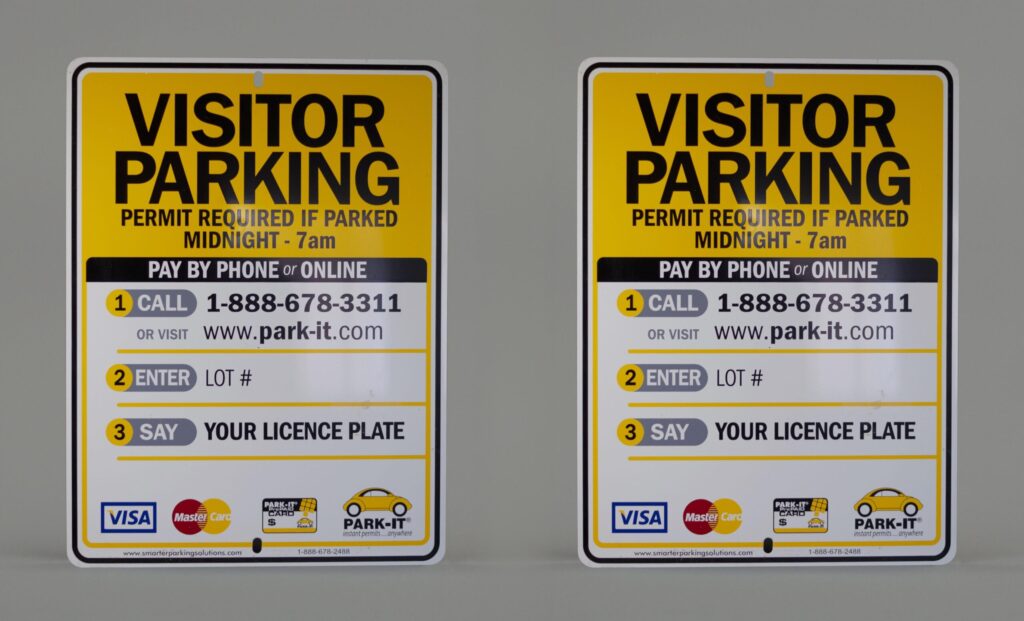Two identical visitor parking signs displaying the different rules and regulations about parking in that particular spot including phone numbers websites, reminder of license plate and payment options