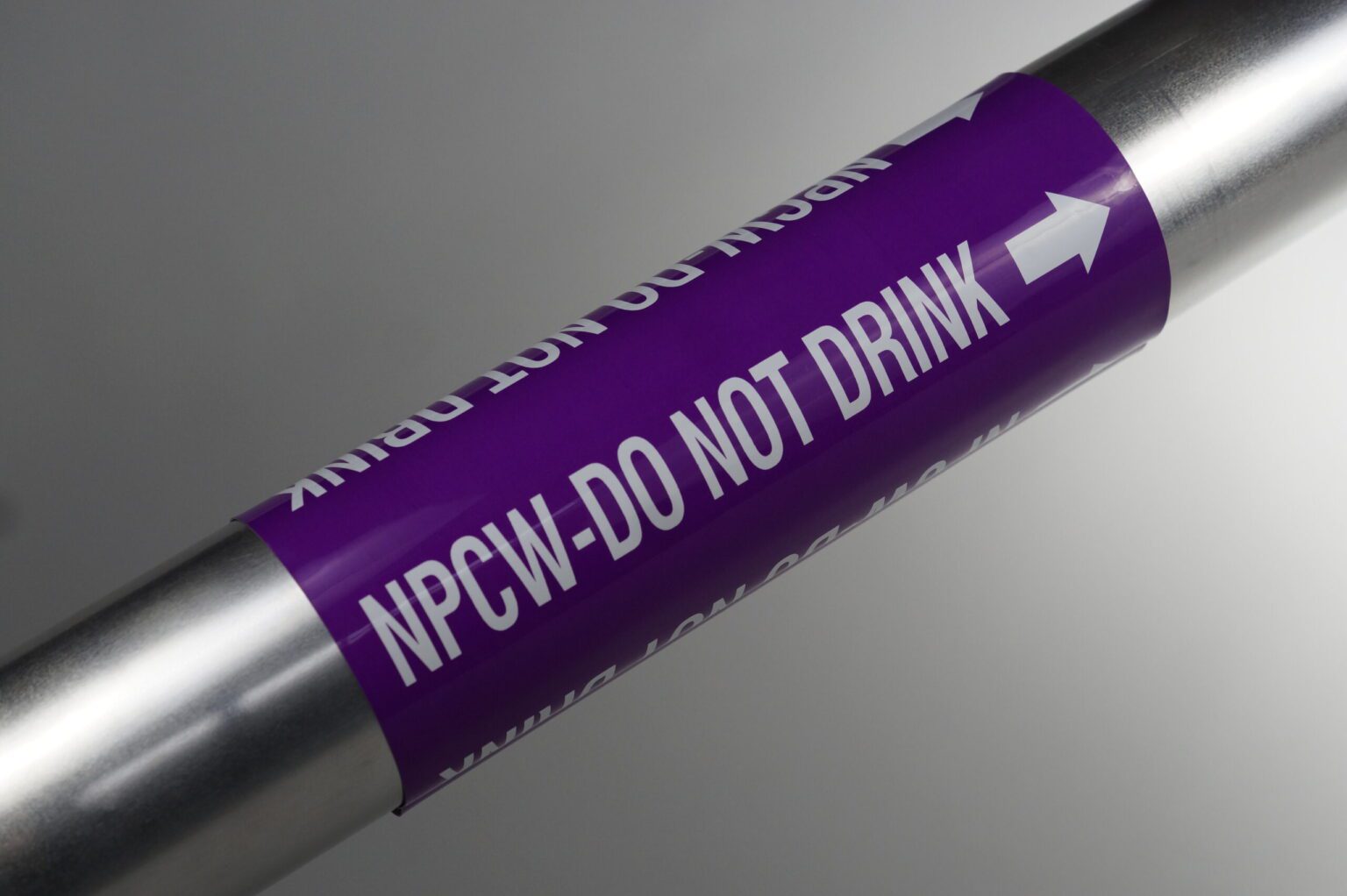 A purple coiled pipe marker wrapped around a steel pipe. The legend reads npcw do not drink with an arrow pointing to the right