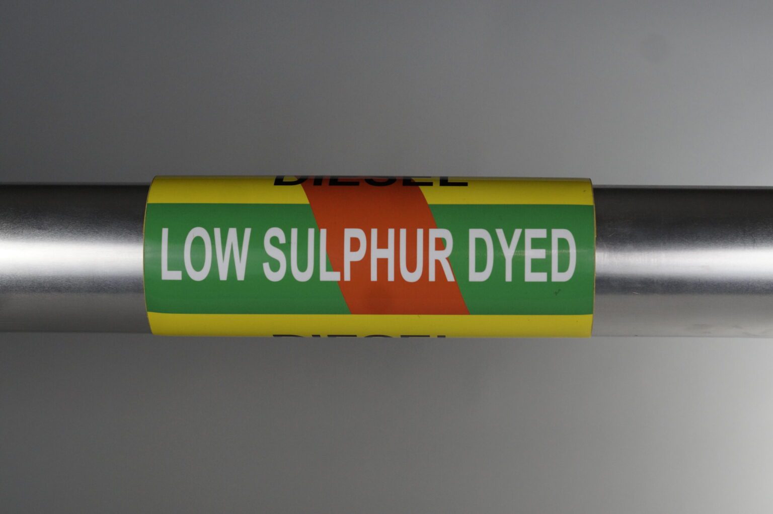 A yellow coiled pipe marker wrapped around a steel pipe. There is a green band going through the middle and a red stripe going through as a diagonal. The legends on the top and bottom read diesel and the legend in Plain view reads Low sulphur dyed.