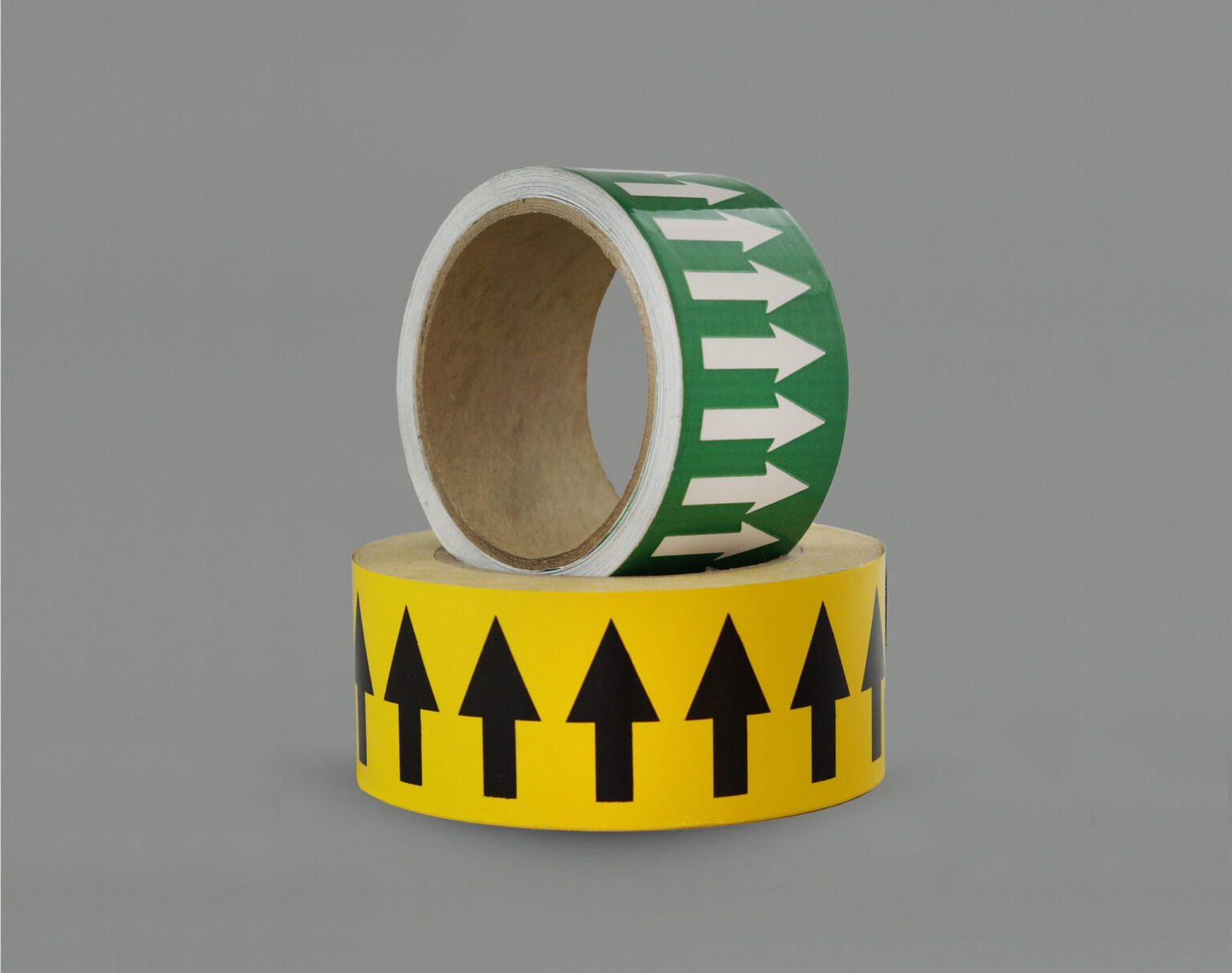 A yellow arrow tape roll sits flat with its arrows pointed up. Nested inside is a green arrow tape roll with its arrows pointing to the left
