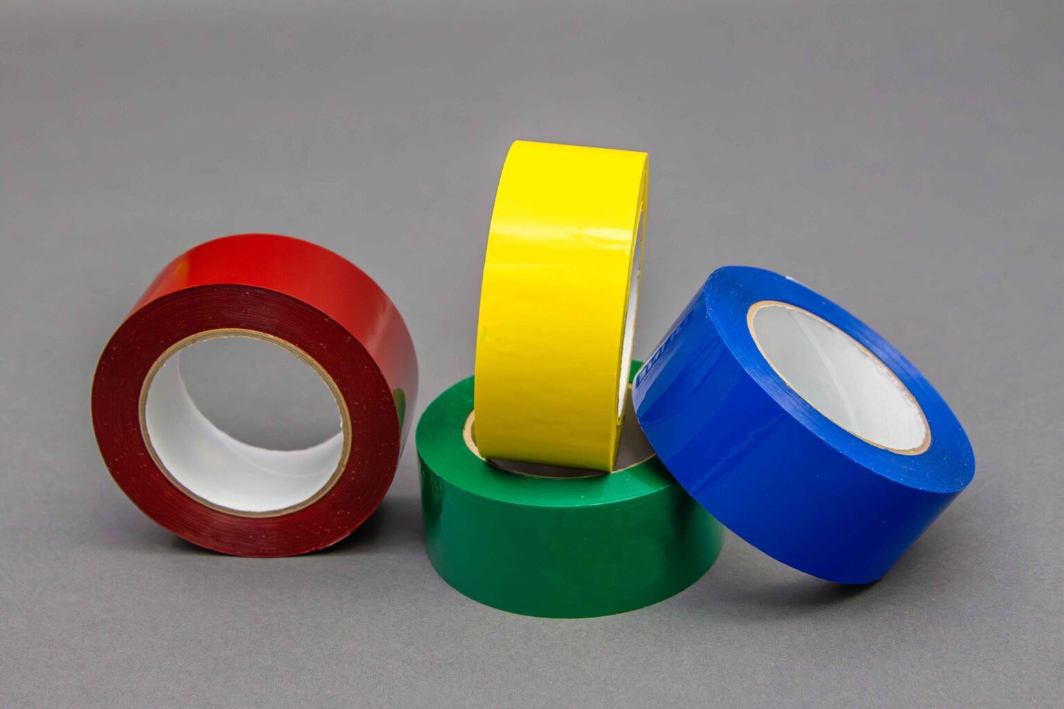 Four banding tape rolls are displayed nicely on a clean gray background. The first roll is red, the second roll is green, the role beside that is yellow and the final roll is blue
