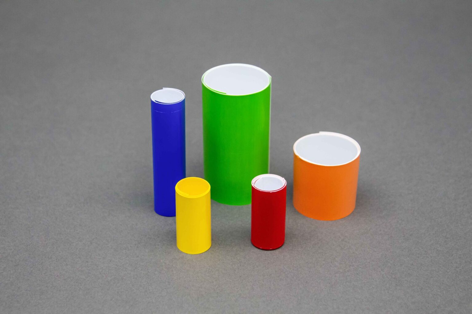 Five Short coiled conduit markers of different widths and colors stand vertically against a clean gray background