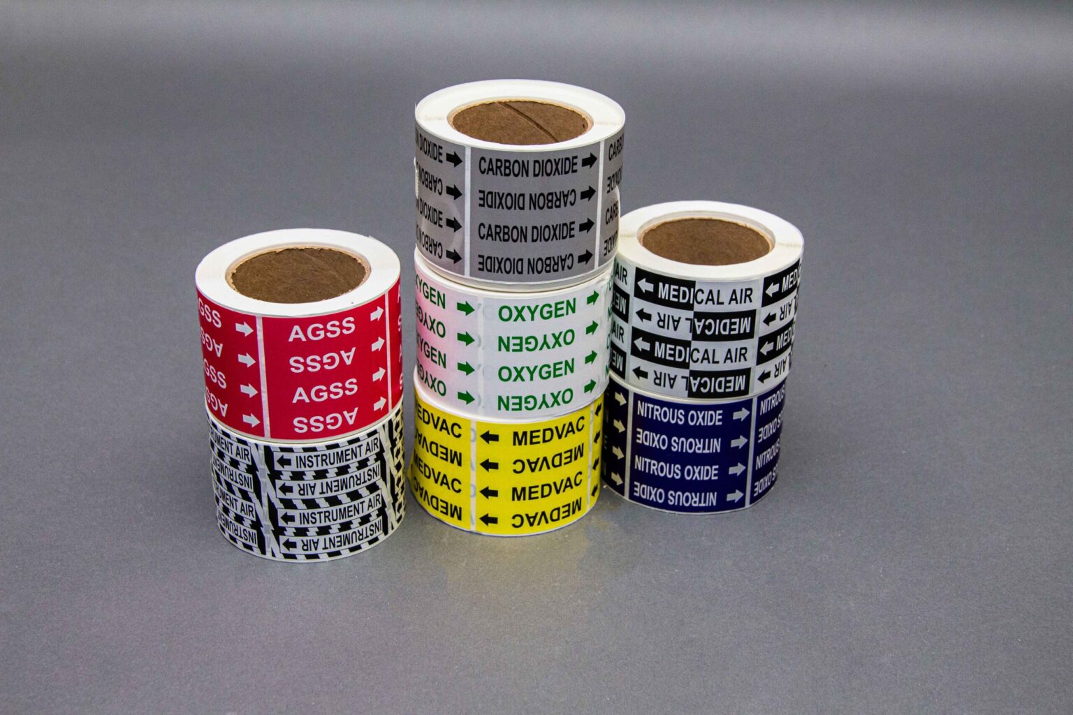 Seven rolls of medical pipe labels two rolls on the left, three roles in the middle, and two rolls to the right. Showcasing the different colors, reflective styles, and legends.
