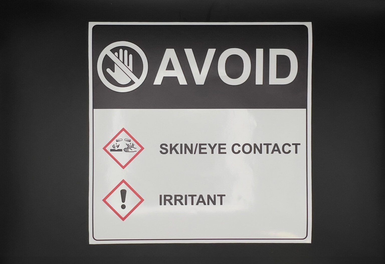 A white sticker that has a black section at the top with an don't touch icon next to the word avoid in white. Below that is the women's symbol for skin and eye contact and irritant