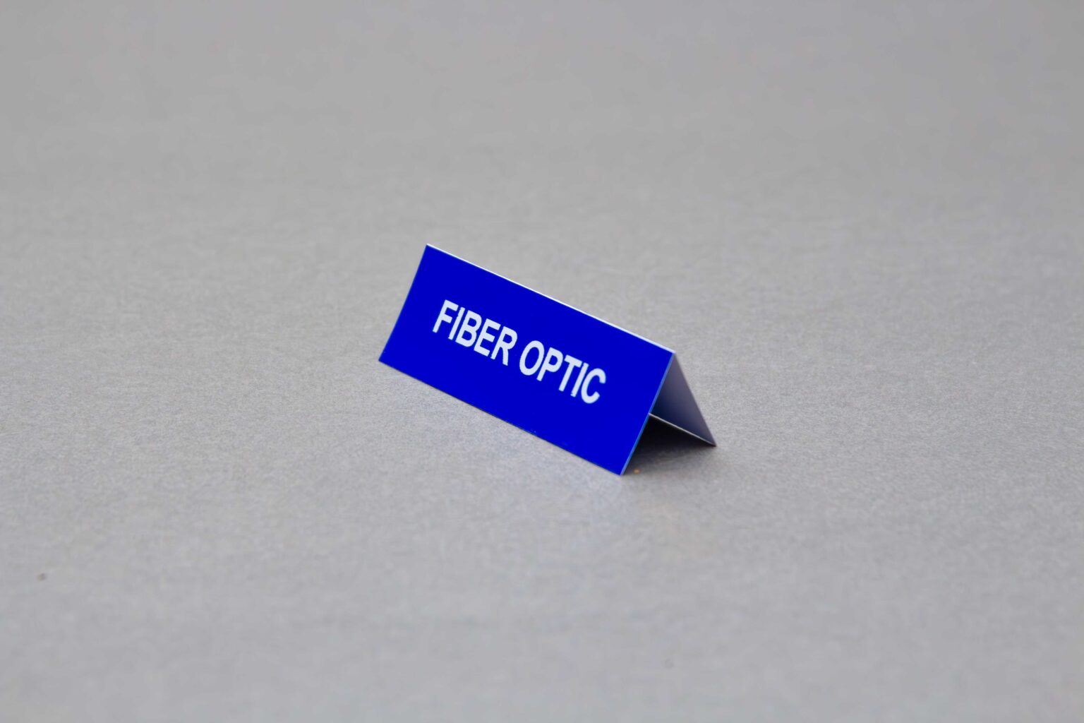 A small blue adhesive conduit marker sticker that reads fiber optic on a 45° angle