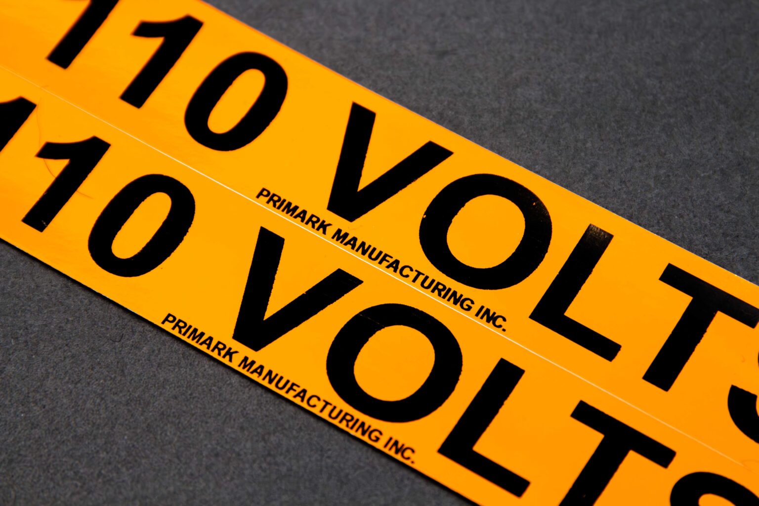 A close up of an orange sticker that reads 110 volts in Black text on a 45° angle