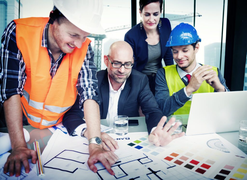 A group of four people in a high-rise office looking at different color schemes and layout options two of them are wearing reflective vests and hard hats. There is a crane outside of the window in the background